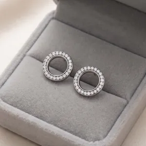 Close-up van zilveren pavé kristallen holle cirkel oorknopjes in een grijze fluwelen doos.
