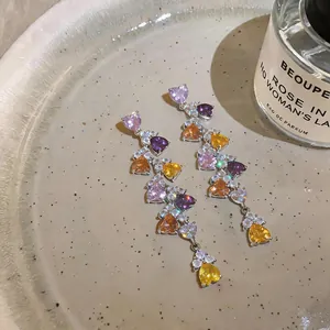Detailed macro view of colorful heart-shaped zircon tassel earrings on a ceramic plate