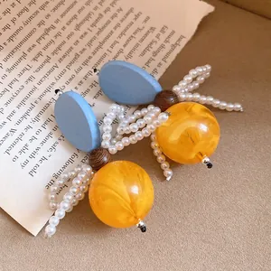 Macro detail of vintage earrings with blue wood elements and orange resin spheres.