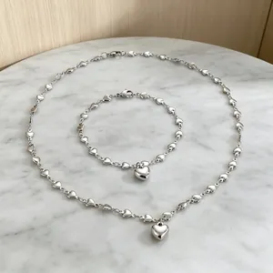 Elegantes silbernes Herz-Halsketten- und Armband-Schmuckset auf einer weißen Marmorfläche