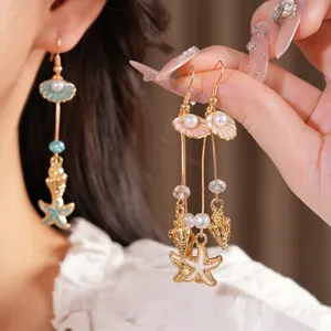 Detailed macro view of gold-tone beach-themed earrings featuring shell, starfish, and pearl charms
