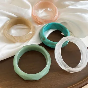 Eleganti bracciali rigidi in acrilico sfaccettato con motivi marmorizzati su vassoio legno