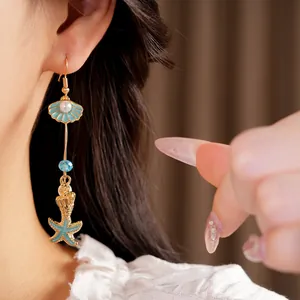 Detail view of marine themed drop earrings featuring shell, conch, and starfish charms.
