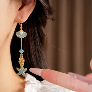 Detailed close-up of blue enamel starfish and shell drop earring worn by a model