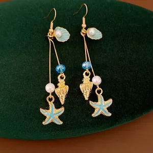 Detailed macro shot of vacation-style starfish and seashell pearl drop earrings.