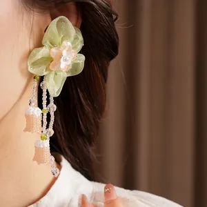 Detailed close-up of a green chiffon flower earring with elegant bead tassels worn by model.