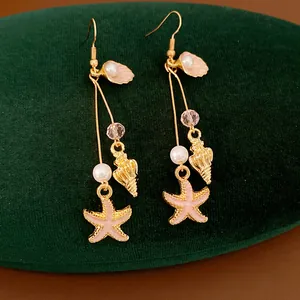 Close-up detail of pink starfish and shell gold-tone drop earrings with elegant pearls