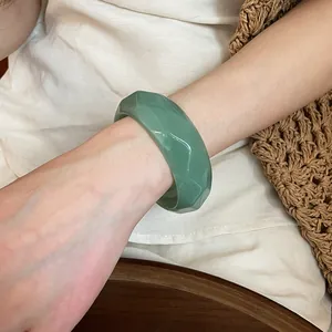 Dettaglio ravvicinato di un elegante bracciale rigido in acrilico sfaccettato verde al polso.
