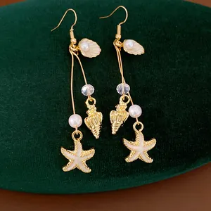 Detailed view of gold drop earrings with starfish and shell charms on green velvet