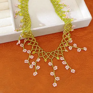 Detail of handmade boho beaded floral necklace with green mesh and pink flowers.
