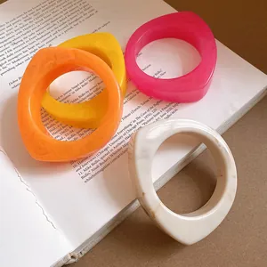 Macro view of colorful geometric resin bangles with marble textures displayed on a book