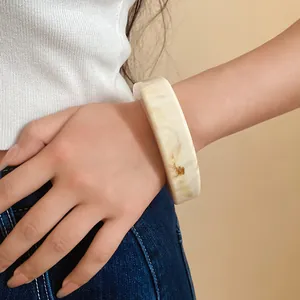 Close-up detail showing the marbled cream resin texture of this geometric bangle on a wrist