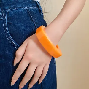 Detail view of a vibrant orange resin geometric arc bracelet worn on a female wrist