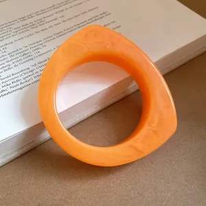 Detail of orange marbled resin bangle with geometric teardrop shape on white book