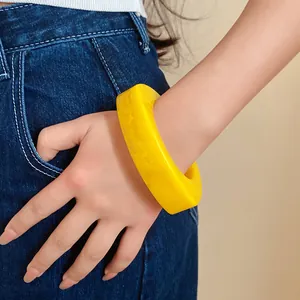 Detailed view of a thick yellow resin bangle with geometric curved design on wrist