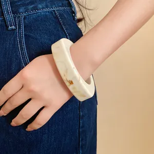 Detail view of a chunky resin bangle bracelet with yellow marbled pattern on wrist.