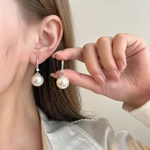 Close-up detail of an elegant pearl drop earring with zircon flower design worn on model's ear