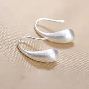 Macro view of minimalist matte silver teardrop hook earrings on a textured fabric surface