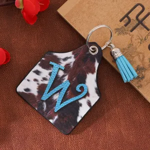 Close-up of western cowhide print ear tag keychain with blue letter W and tassel.