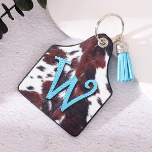 Detail view of cowhide pattern leather ear tag keychain with blue letter W and tassel.