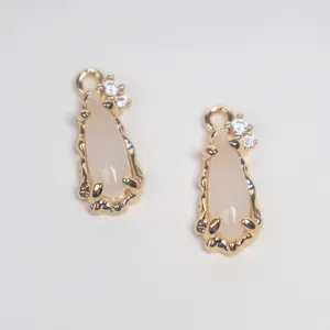 Detailed macro view of gold-plated copper teardrop charms with white glass and zircon