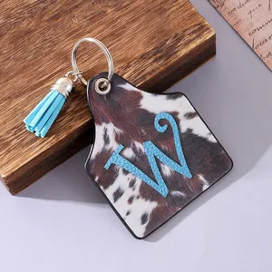Close-up of western-style cow print farm tag keychain with blue tassel and letter W detail