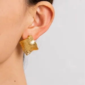 Detailed macro shot of a gold textured irregular square earring worn on a female model's ear