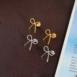 Detail shot of elegant gold and silver stainless steel bow earrings on leather.