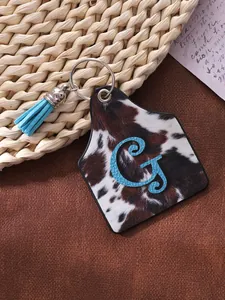 Close-up of a western style cowhide print leather keychain with blue tassel and letter G