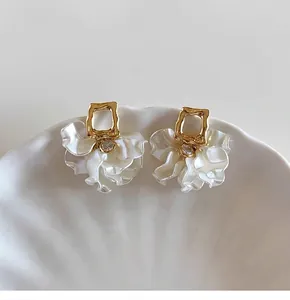 Close-up view of elegant French style gold earrings with white petal charms and rhinestones.