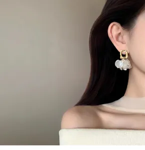 Detailed close-up of elegant gold geometric earrings with delicate white petal dangles on a model