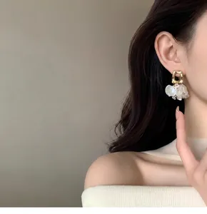Detailed close-up of French-style golden petal pearl drop earrings on a model's ear