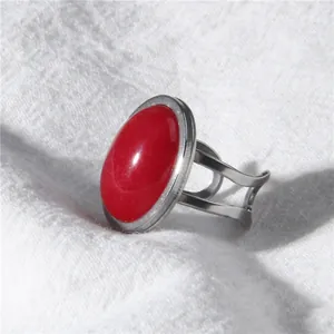 Macro view of a minimalist silver ring featuring a bold red oval stone on textured fabric.
