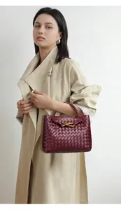 Vista dettagliata di una modella con borsa tote intrecciata a mano bordeaux e fiocco dorato.