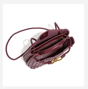 Dettaglio interno di una borsa tote in pelle intrecciata bordeaux con nodo dorato.