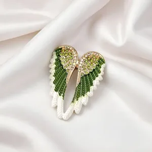 Close-up detail of a green enamel angel wing brooch with rhinestones on white satin