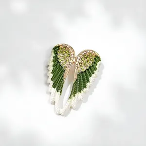 Close-up of elegant green and white enamel angel wing brooch with rhinestones