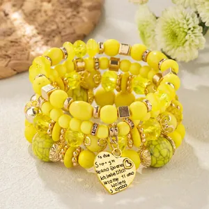 Close-up of yellow bohemian beaded bracelets featuring a multi-language heart charm