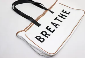Detail view of large white canvas tote bag with BREATHE print and brown piping trim