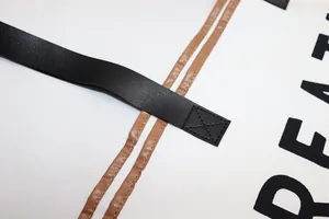 Detailed view of black leather strap and stitching on large white canvas beach tote bag