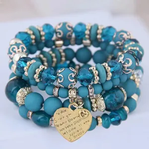Close-up detail of teal Bohemian layered beaded bracelets featuring a gold heart charm