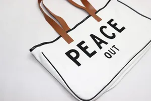 Detail view of a white canvas tote bag with 'PEACE OUT' print and brown handles