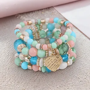 Close-up of Bohemian layered beaded bracelets with an engraved golden heart pendant.