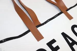 Close-up of the brown leather handle and reinforced stitching on a white canvas tote bag