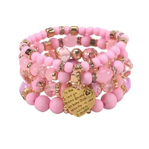 Close-up detail of pink beaded stacking bracelets featuring an engraved gold heart charm