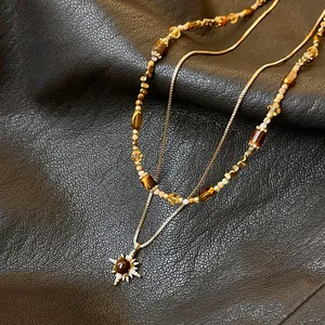 Close-up of layered tiger eye necklace with golden sun pendant on black leather surface.