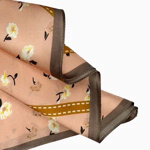 Detail macro view of elegant peach silk square scarf with floral print and brown border.