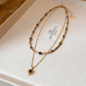 Detailed view of a double-layer gold necklace with tiger eye beads and sun pendant.
