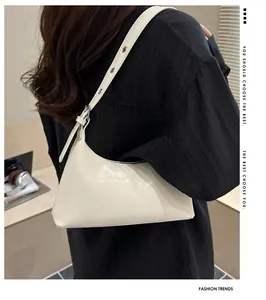 Glossy white underarm baguette bag worn by a model in a modern office setting.