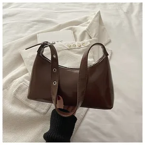 Detailed view of a brown glossy underarm handbag featuring an adjustable eyelet strap